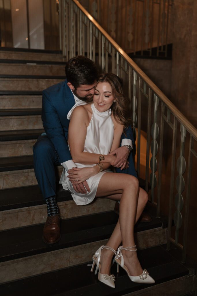 Engaged couple sitting on the grand staircase at The Cardinal Hotel in Winston Salem, wrapped in an intimate embrace during their engagement session