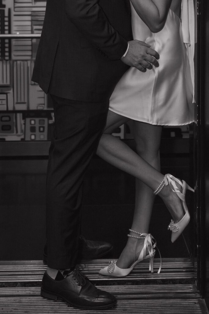 Close-up black and white photo of an engaged couple’s legs and shoes as they embrace in an elevator at The Cardinal Hotel in Winston Salem, NC