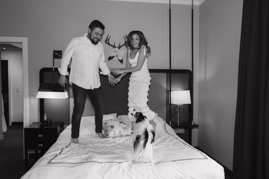Engaged couple jumping on the bed inside the Kimpton Cardinal Hotel in Winston Salem, NC