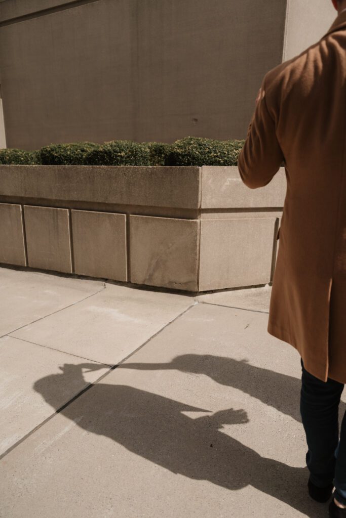 Artistic shadow of an engaged couple holding hands on a sidewalk outside The Cardinal Hotel in Winston Salem, NC